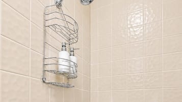 Un bagno con piastrelle color crema, una doccia con soffione estraibile, un portasciugamani e una barra di sostegno.