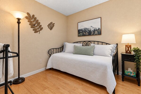 A bedroom with a bed, a nightstand with a lamp, a wall-mounted plant, and a painting.