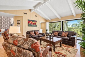 A spacious living room with two sofas, a coffee table, and a large window offering a view of trees.