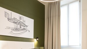 A modern bedroom with a large bed, a bedside table, a headboard, a window with curtains, and a wall-mounted artwork. - Porta Antica (Bergamo)