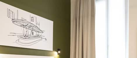 Un dormitorio moderno con una cama grande, una mesita de noche, cabecero, una ventana con cortinas y una obra de arte colgada en la pared.