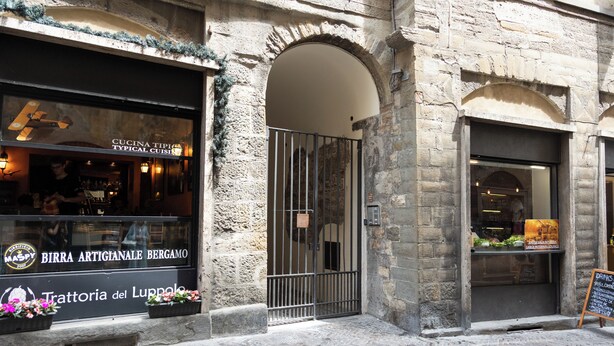 A stone building with a storefront featuring a sign for 'Cucina Tipica' and 'Birra Artigianale Bergamo'. - Porta Antica (Bergamo)