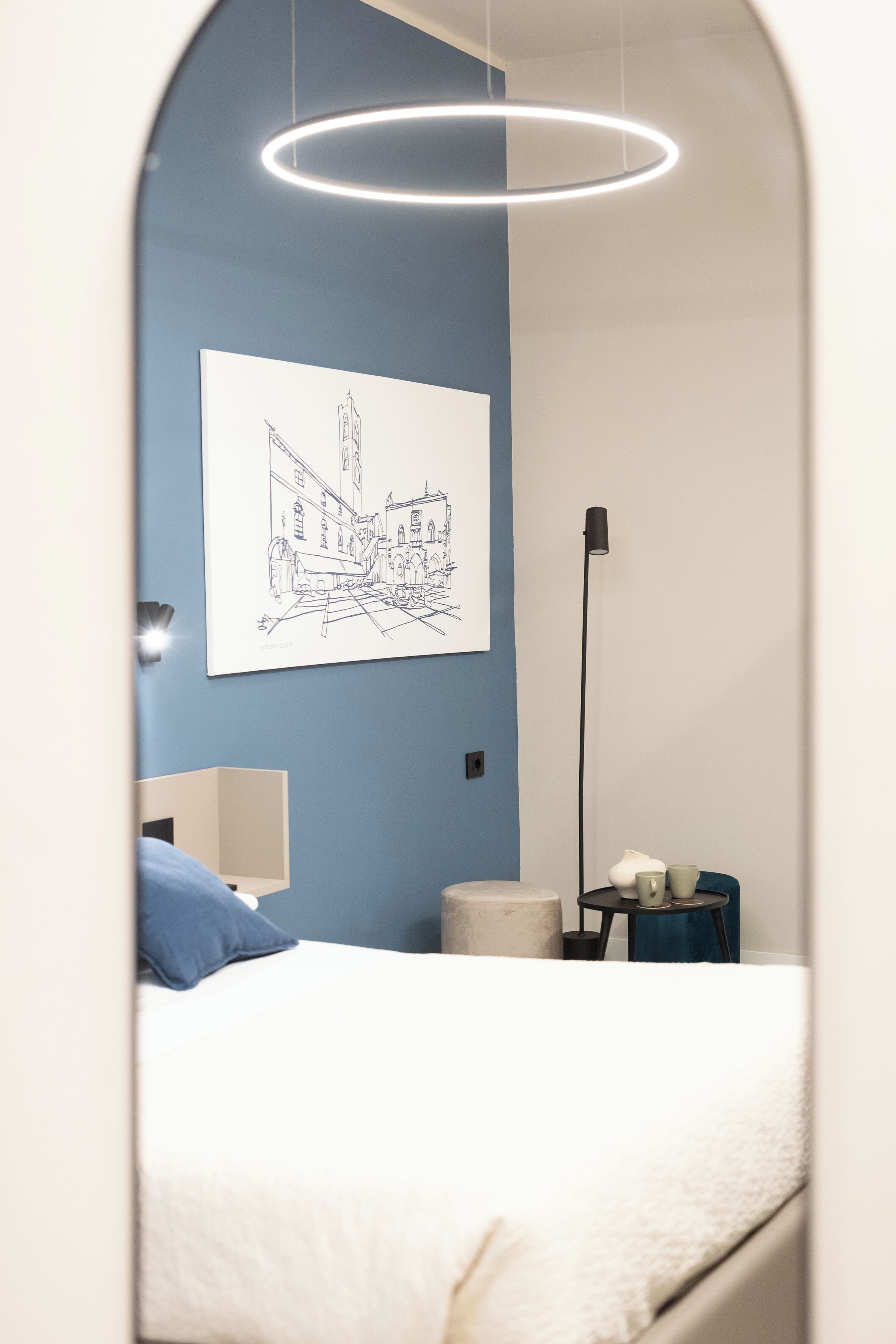 A bedroom with a bed, a bedside table, a lamp, and a wall-mounted artwork.