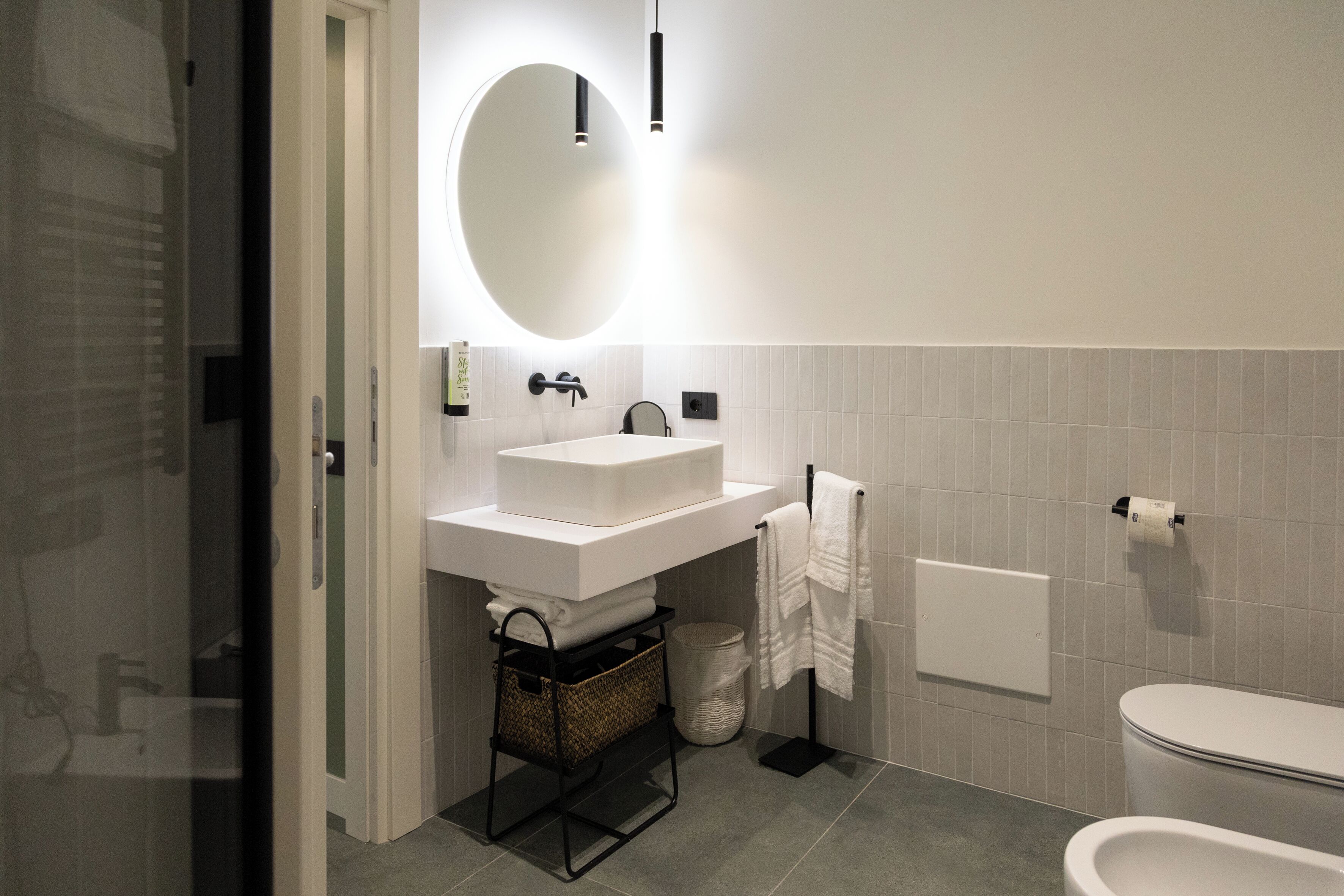A modern bathroom with a white sink, a large mirror, a towel rack, and a toilet.