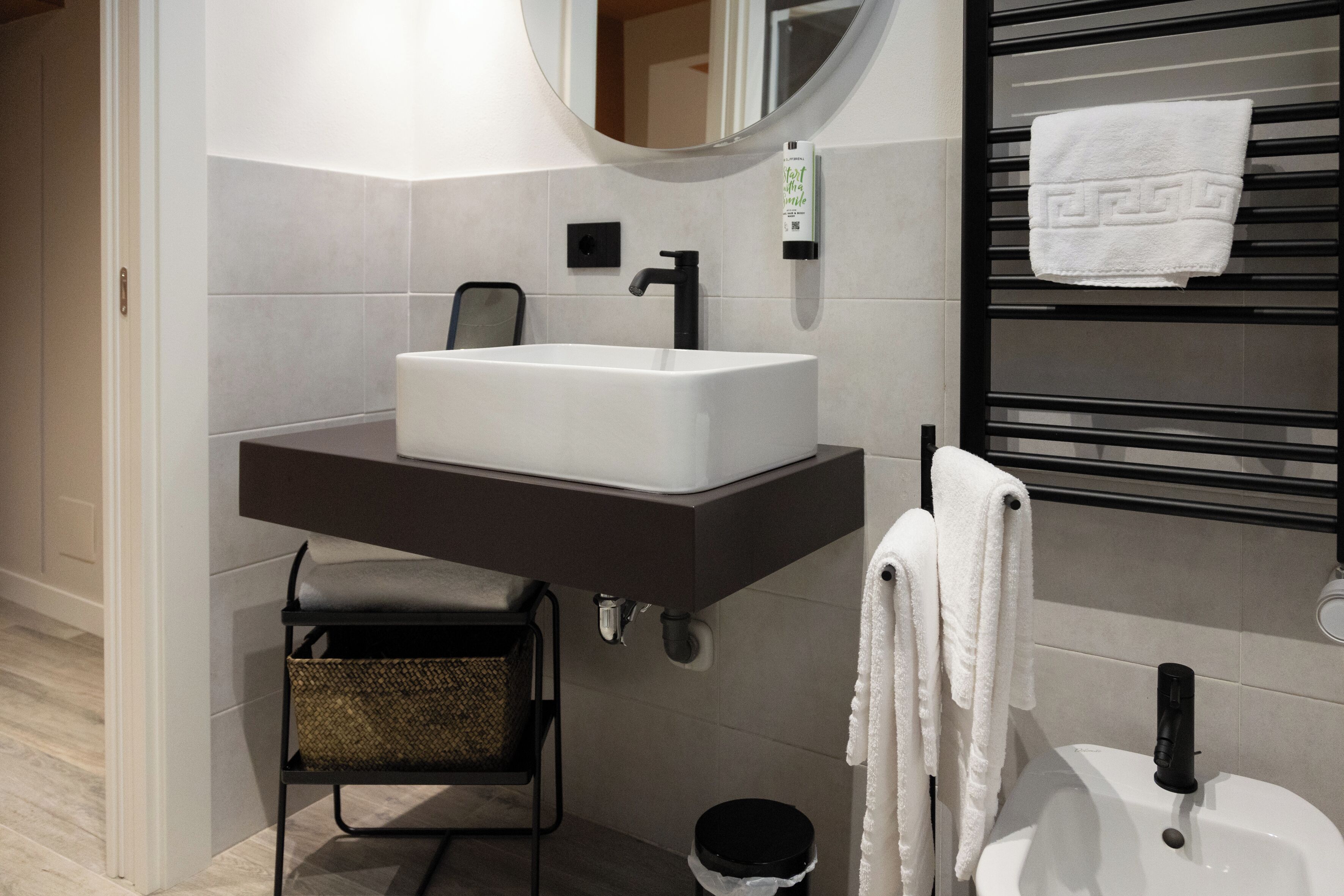 A modern bathroom with a white sink, black towel rack, and a small stool.