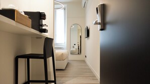 A narrow hallway with a black chair, a small sofa, a mirror, and a shelf with a coffee machine. - Porta Antica (Bergamo)