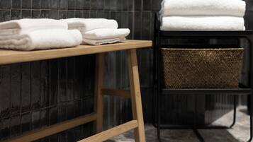 A wooden bench with folded white towels stacked on it and a woven basket on a black metal stand.
