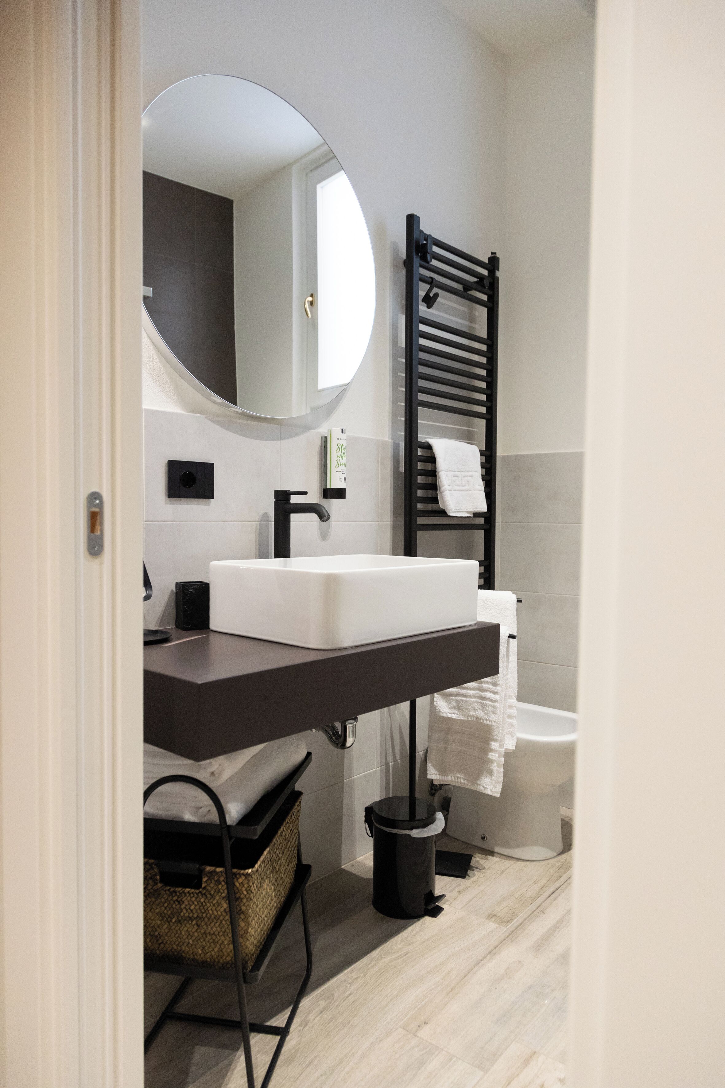A modern bathroom with a white sink, black towel rack, and a round mirror.