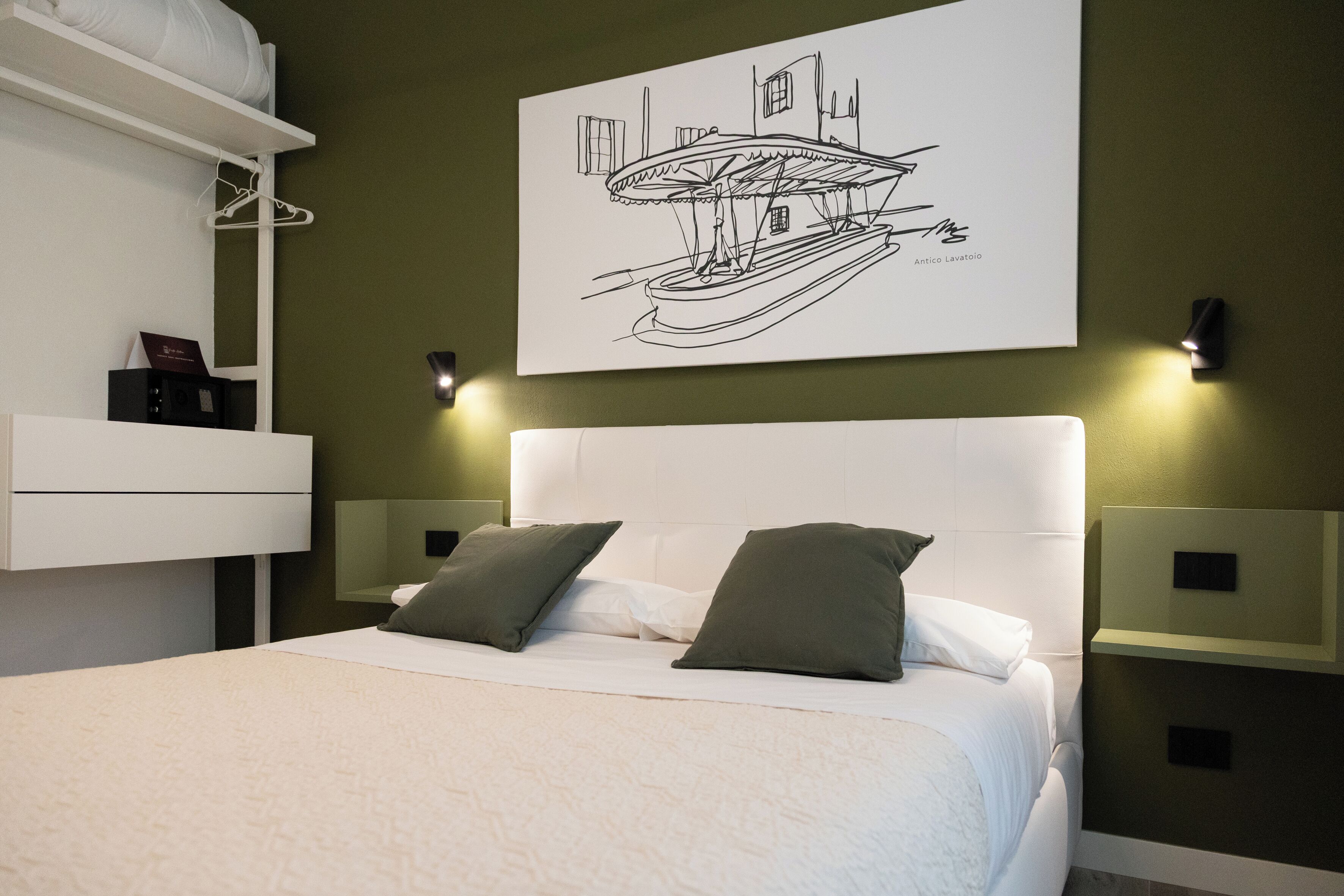 Une chambre d’hôtel moderne avec un grand lit, deux tables de chevet, une armoire blanche et une œuvre d’art fixée au mur représentant un bateau.