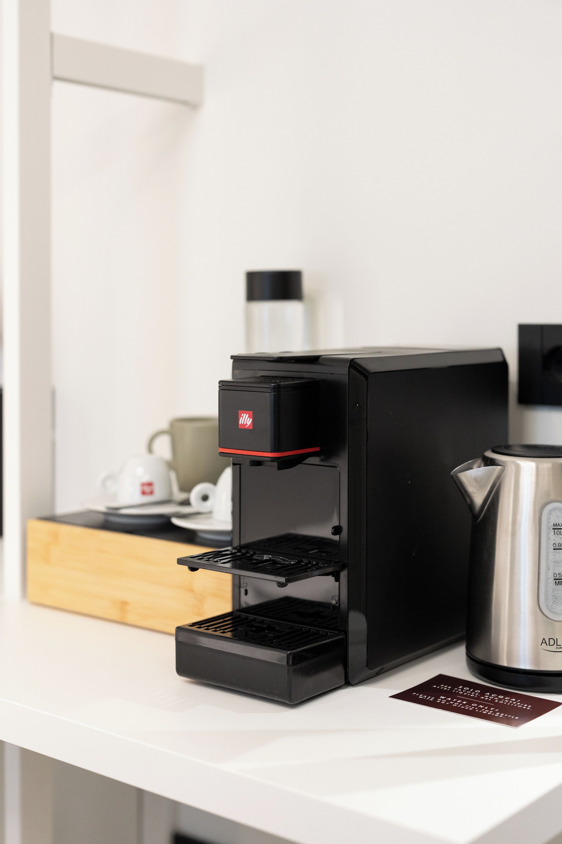 Une machine à café moderne, posée sur un plan de travail blanc, avec une bouilloire en acier inoxydable et une petite assiette.