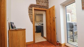 Ein Flur mit einer Holztür, die zu einer Küche mit einer Steinwand und einem Fenster führt.