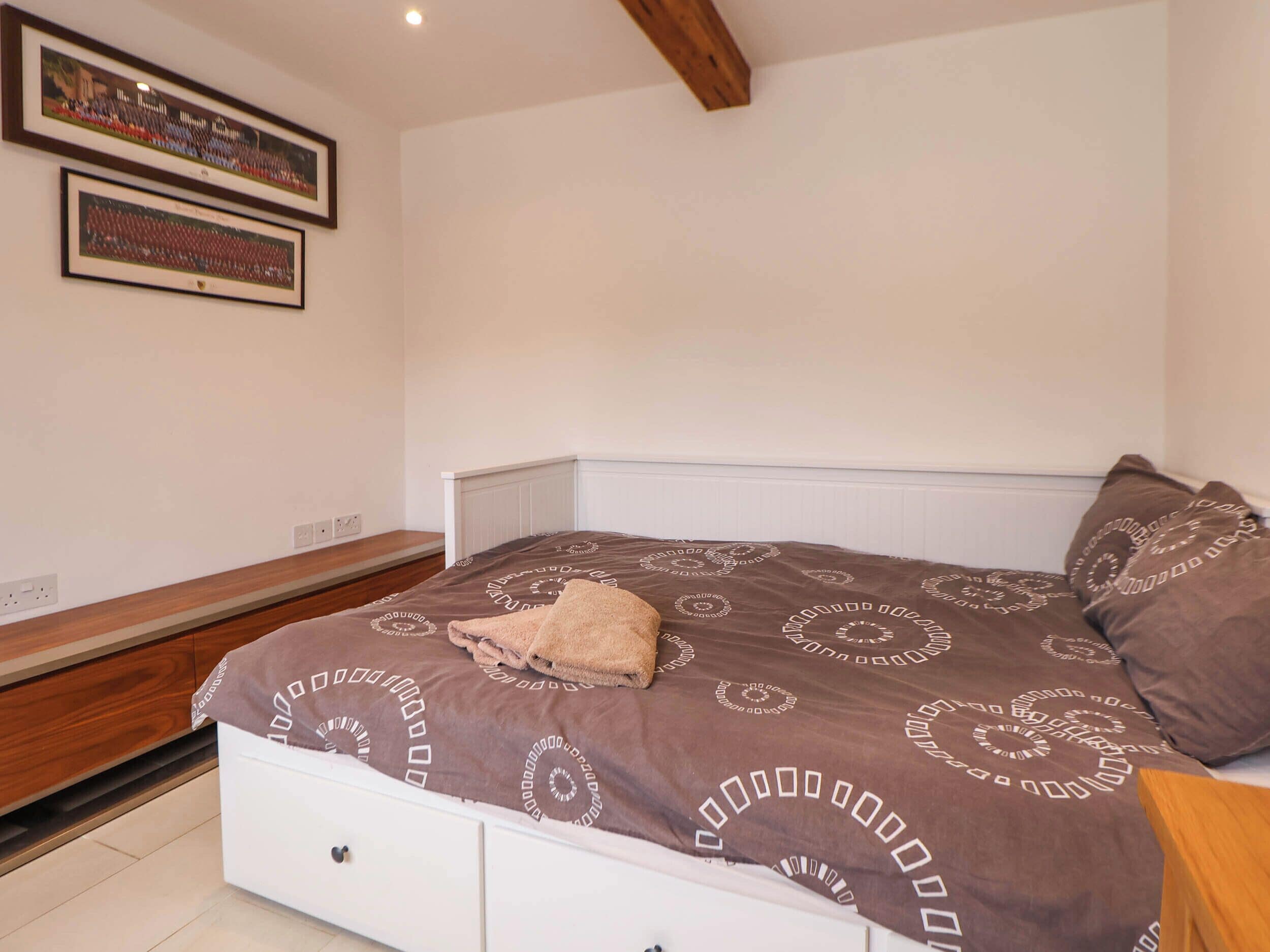 A bedroom with a bed, a bench, and two framed pictures on the wall.