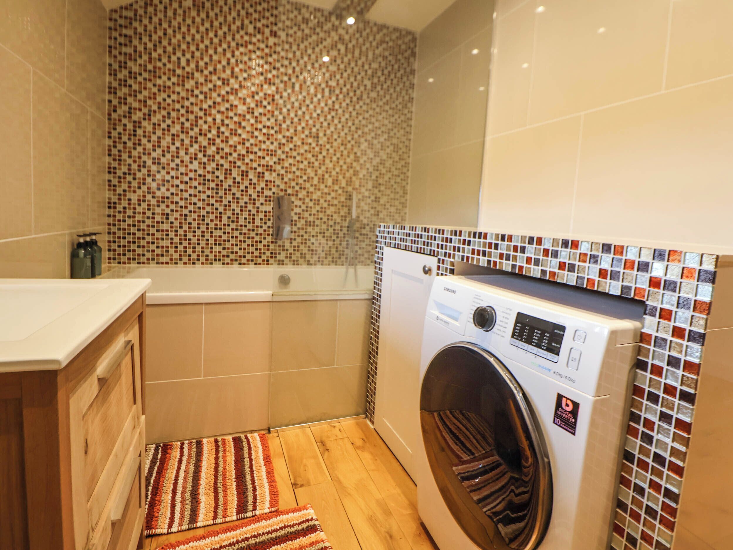 Une petite buanderie comprenant un lave-linge, une baignoire et un mur recouvert de carreaux décoratifs.