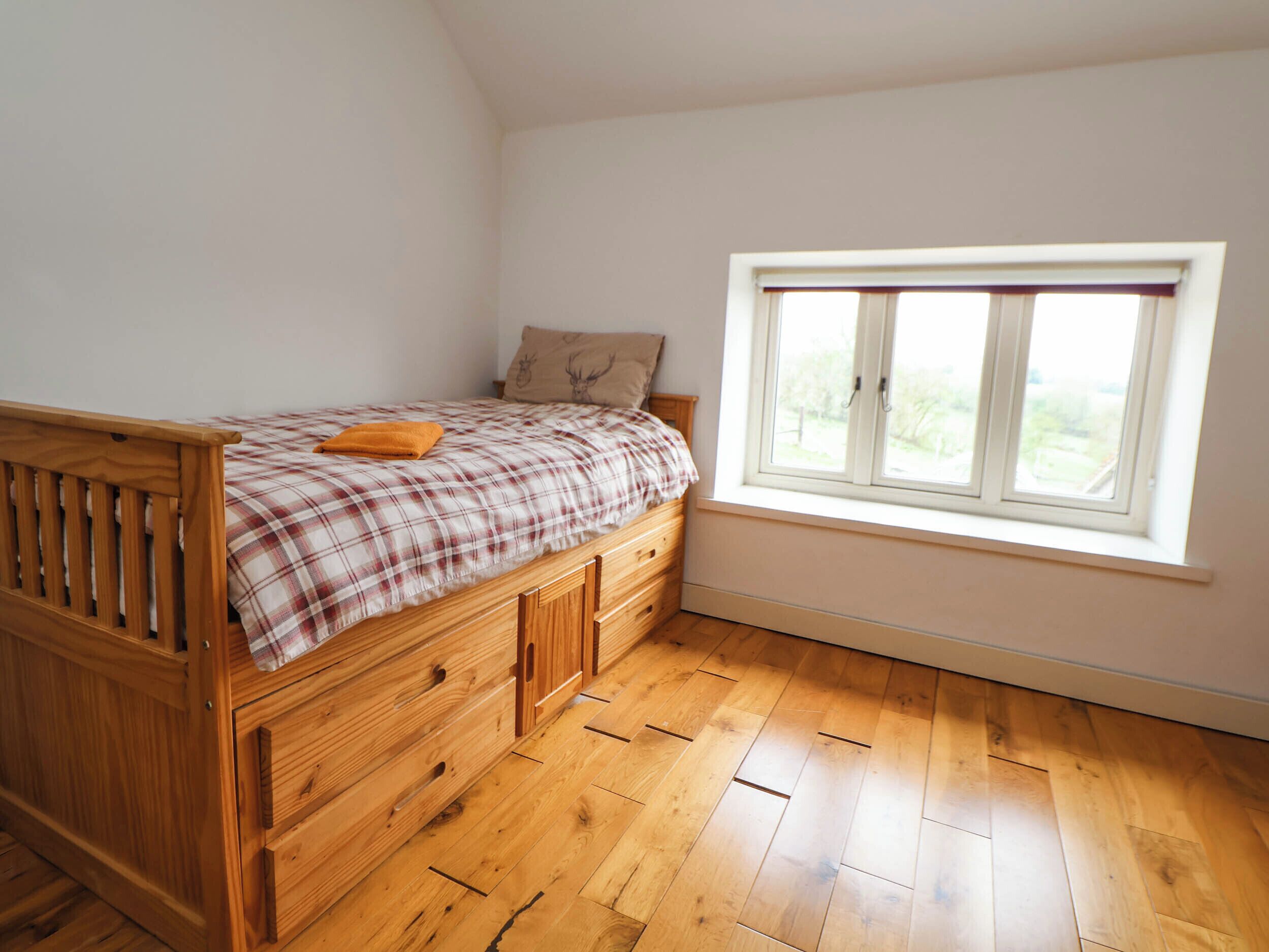 A bedroom with a wooden bed, a window, and a view of greenery outside.
