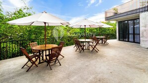Un espace extérieur aménagé en terrasse, avec des tables et des chaises, entouré de verdure et surplombé par un ciel dégagé.