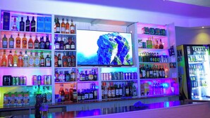 Zona de bar con estantes llenos de botellas de licor, una pantalla de televisión y un refrigerador.
