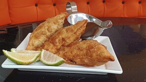 Un plato de pasteles fritos con una cuchara de servir plateada y gajos de lima sobre un plato blanco.