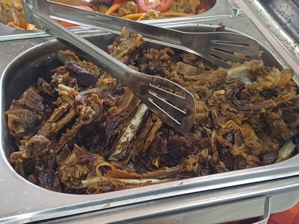 Un bufé con diversos platos, entre ellos carne deshebrada y verduras.
