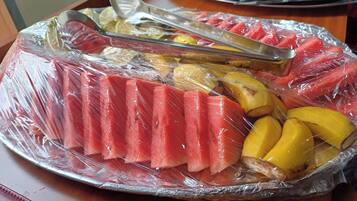 A tray of sliced fruits and vegetables, including watermelon and yellow squash, wrapped in plastic.