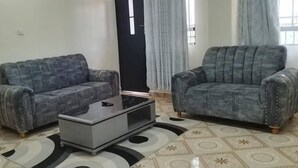 Una sala de estar con dos sofás grises tapizados, una mesa de centro de vidrio y baldosas de suelo con estampado.