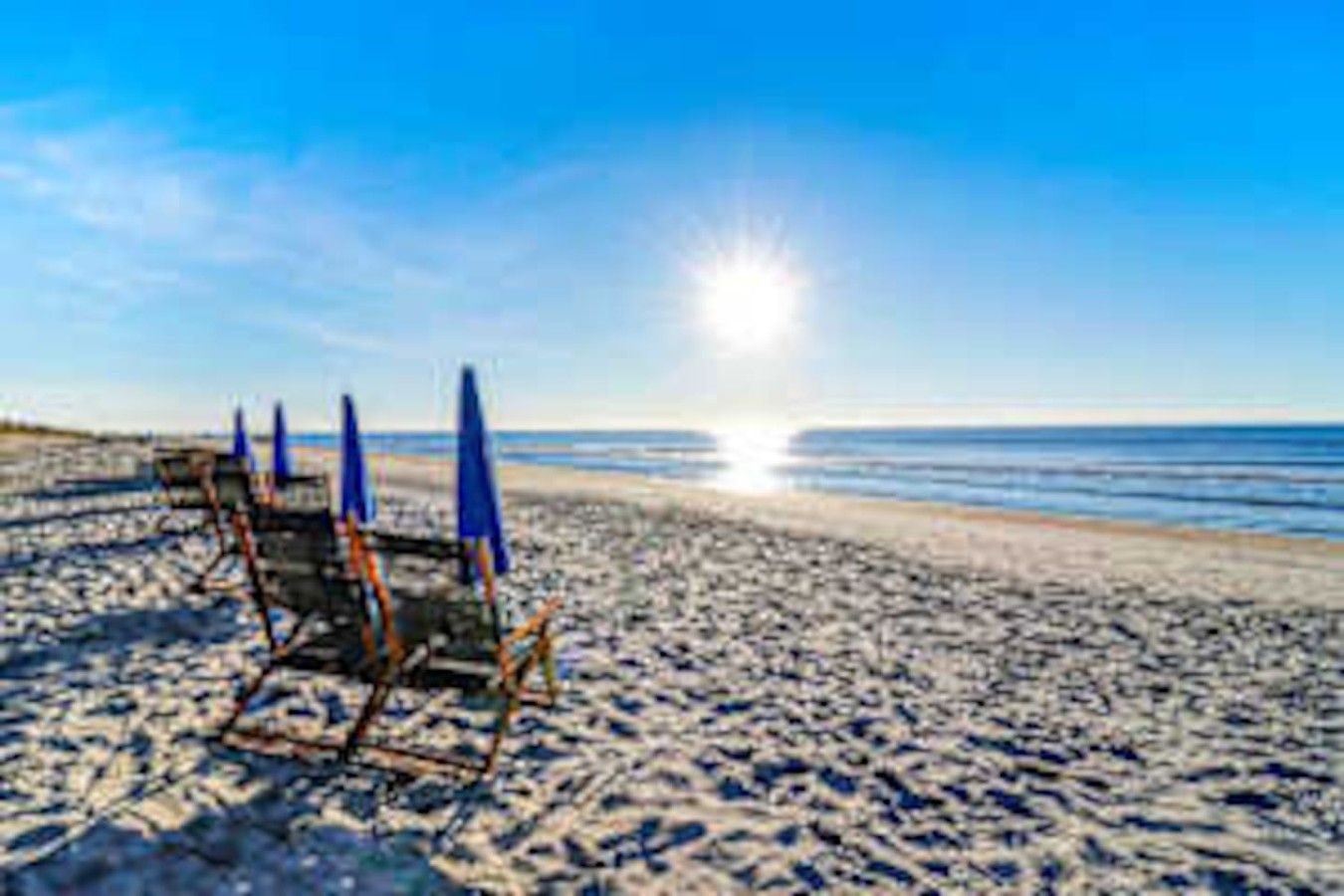 A beach with a row of beach chairs and umbrellas, a clear sky, and the ocean in the background.