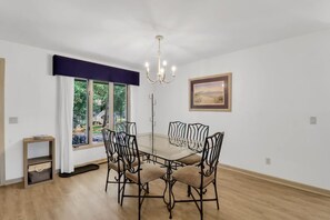 A dining area with a table and chairs, a chandelier, a window with curtains, and a framed picture on the wall.