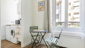 A small, bright room with a washing machine, a table with a chair, and a window with a view of buildings. - Le Petit Palais avec mezzanine au cœur de Cannes (Cannes)