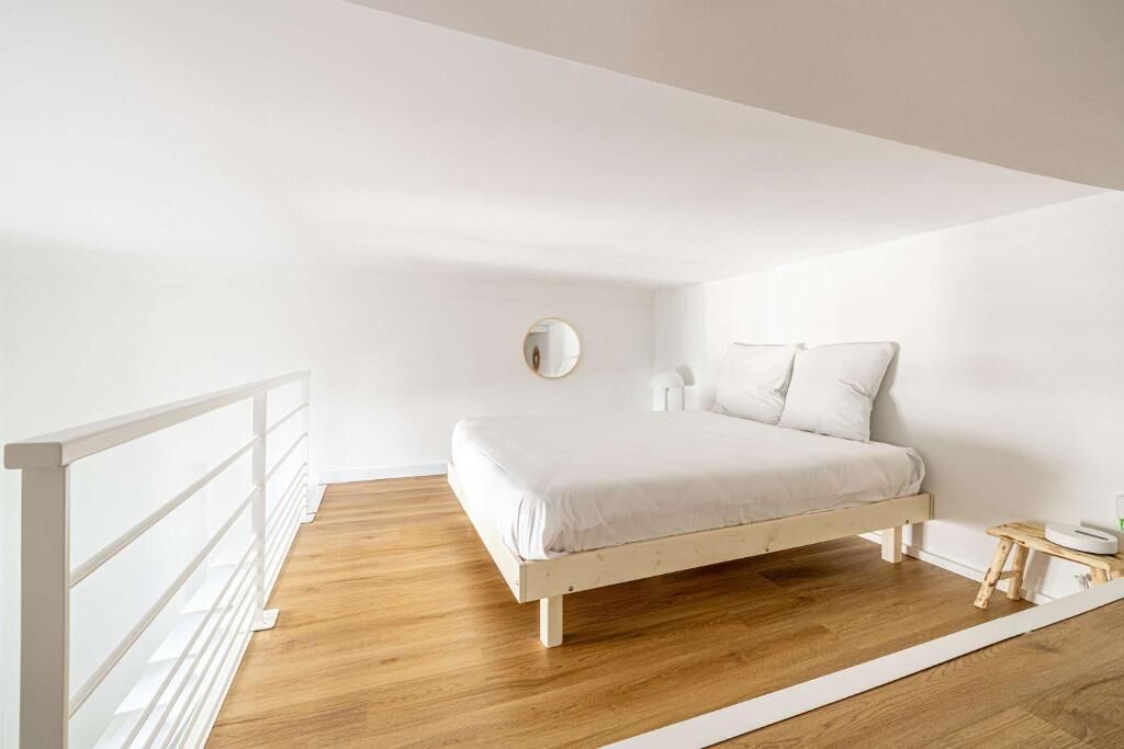A minimalist bedroom with a wooden floor, a white bed, and a white railing.