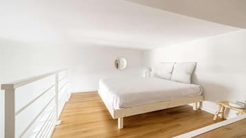 A minimalist bedroom with a wooden floor, a white bed, and a white railing.
