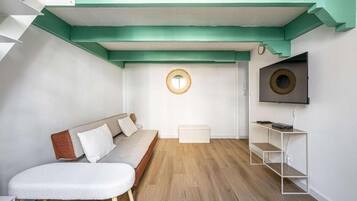 A modern living room with a sofa, a round mirror, a television, and a wooden floor.