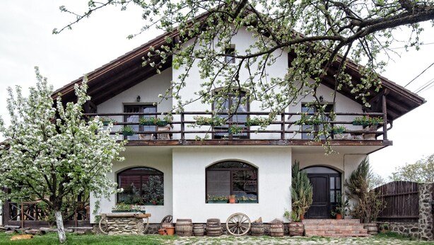 Ein zweistöckiges Gebäude mit Balkon, Steintreppe und einem Garten mit Baum und Topfpflanzen.