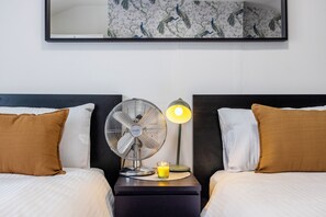Ein Hotelzimmer mit zwei Betten, einem Nachttisch mit Ventilator und Lampe sowie einem an der Wand befestigten Spiegel.