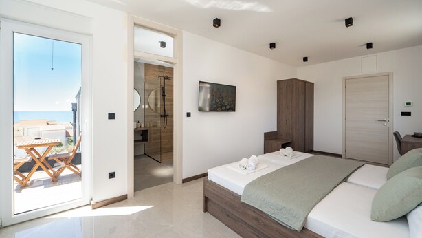 Un dormitorio moderno con cama, un armario de madera y un baño visible a través de una puerta abierta.