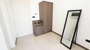 Una habitación con una puerta blanca, un armario de madera, una pequeña mesa con un vaso y un espejo apoyado en la pared.