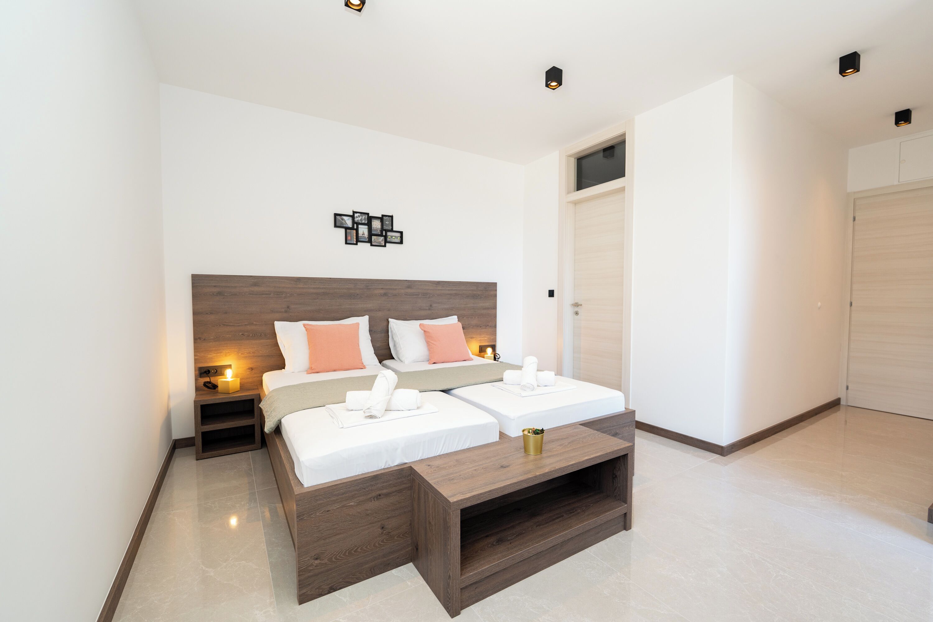 A modern hotel room with two beds, a wooden headboard, a bedside table with a lamp, and a large window.