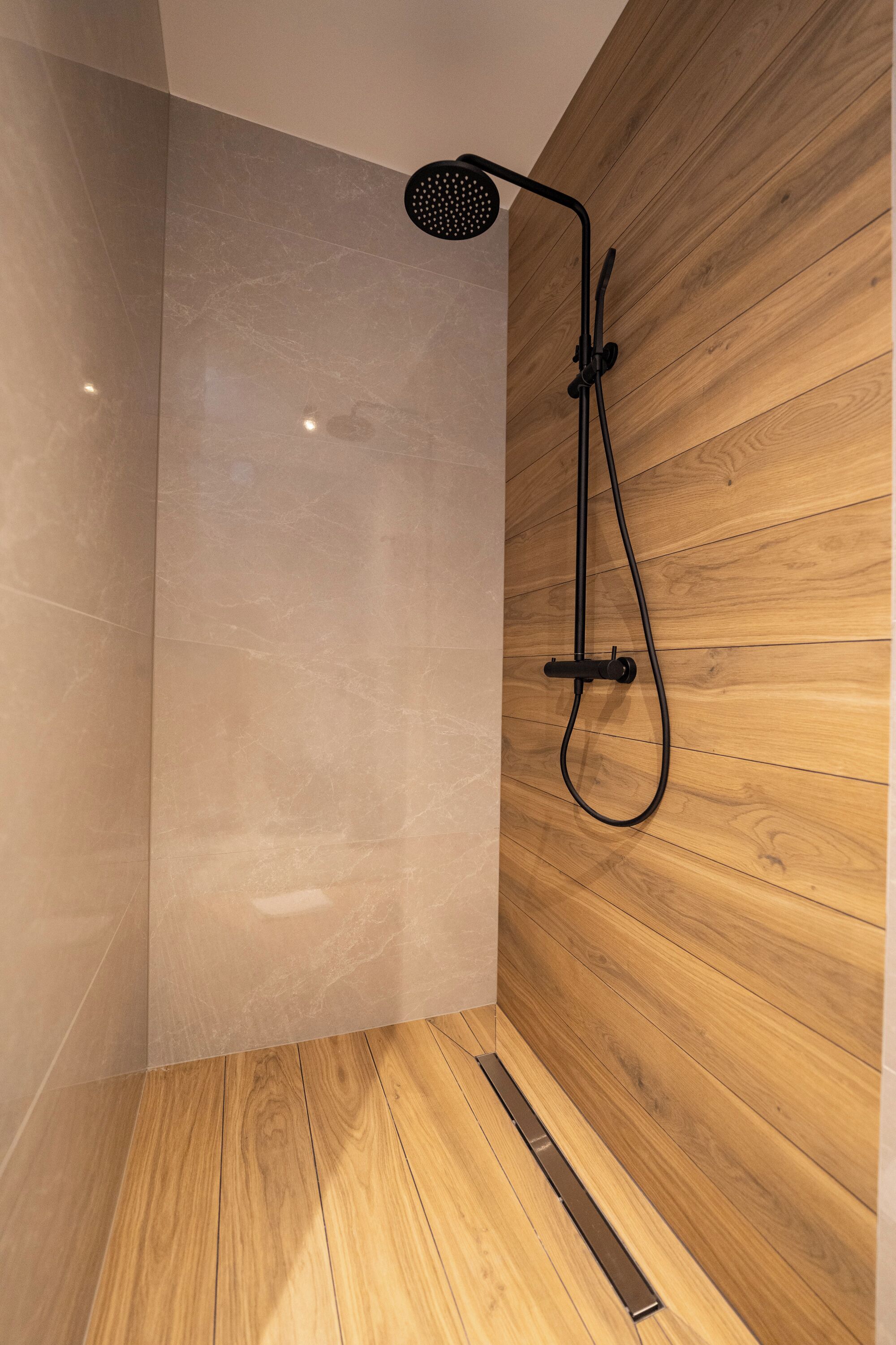 Eine moderne Dusche mit Holzpaneelen an der Wand und einem Marmorboden.