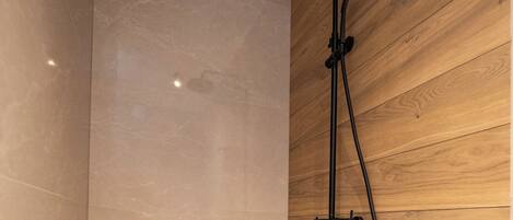 A modern shower with a wooden panel wall and a marble floor.