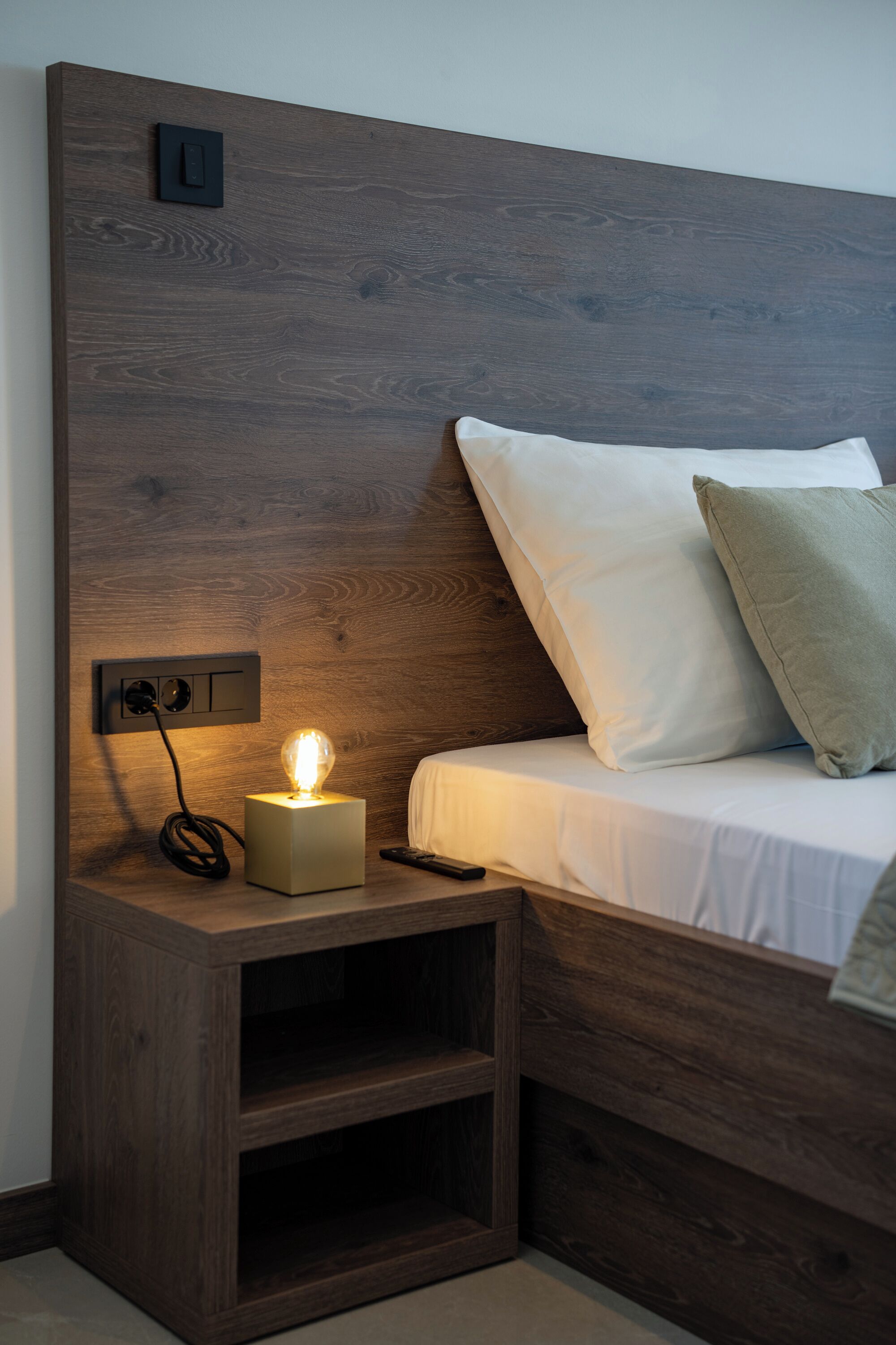 Ein hölzerner Kopfteil mit Nachttisch, Lampe und Fernbedienung.