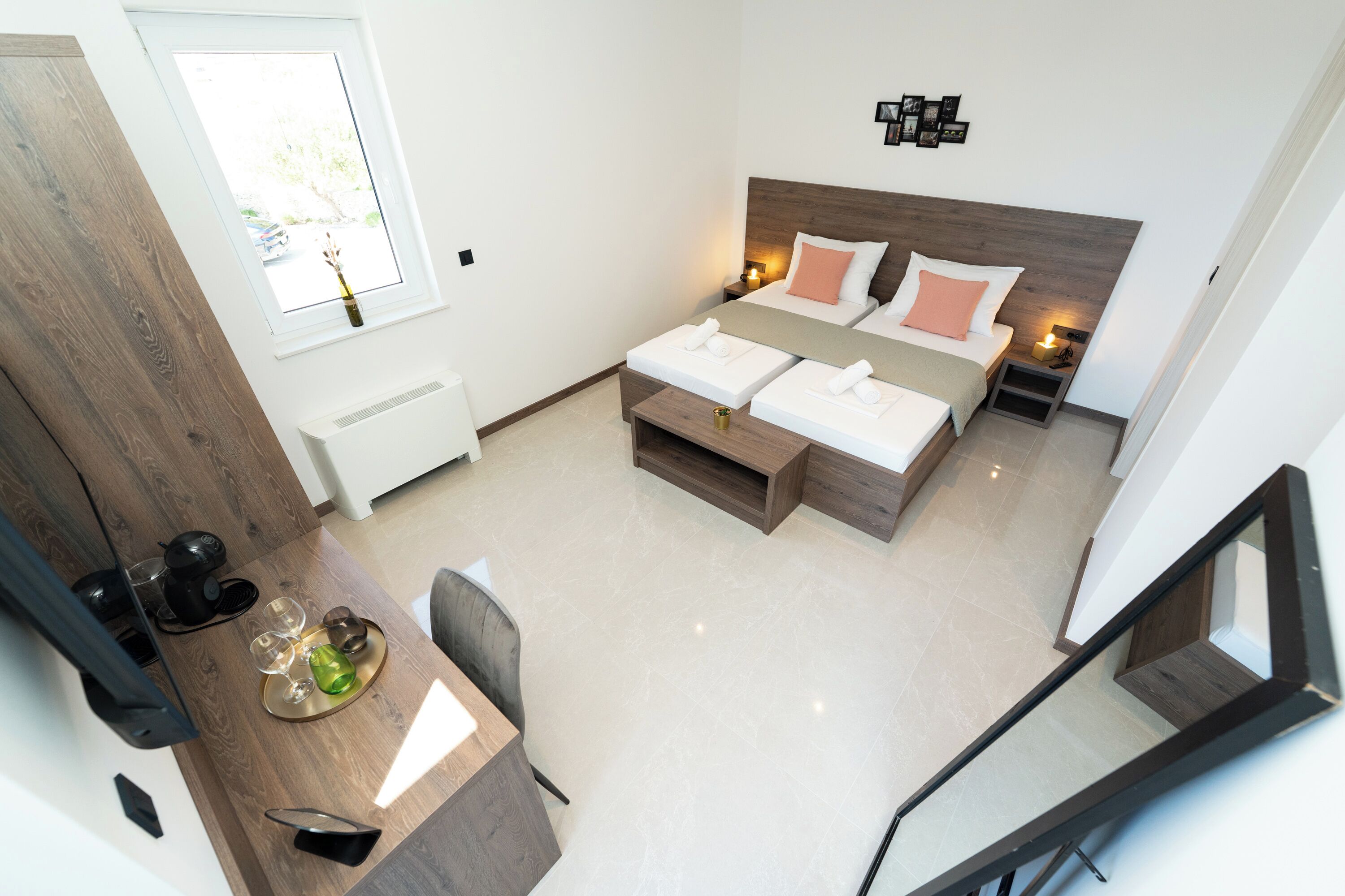 A modern hotel room with a bed, bedside tables, a desk with a chair, and a view of the outside through a window.