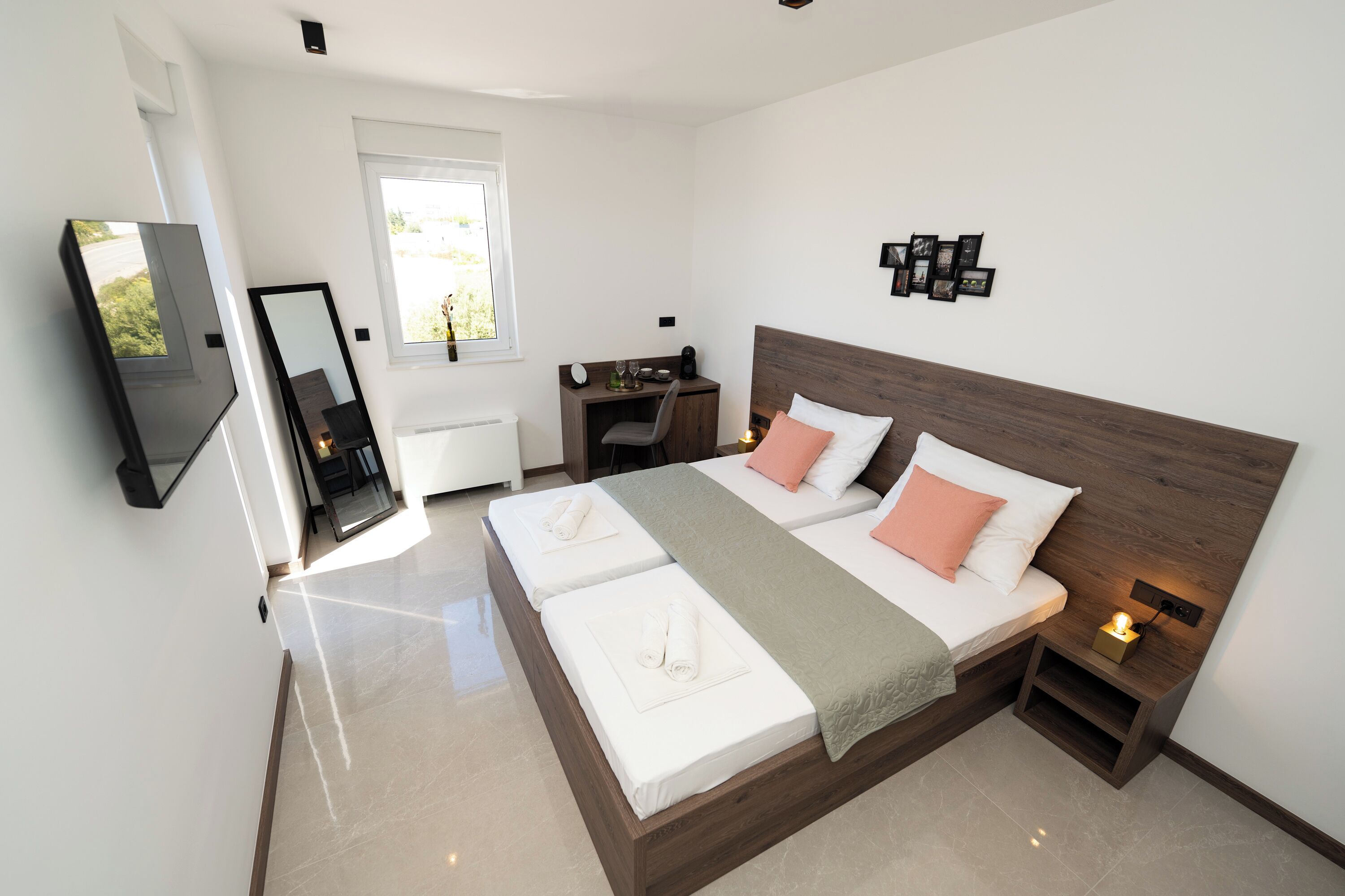 A modern bedroom with a large bed, bedside tables, a desk, and a TV mounted on the wall.