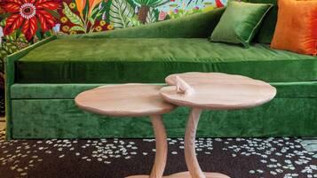 Ein grünes Sofa mit einem runden Holztisch davor, ein lebhaftes Wandgemälde mit Vögeln und Blattwerk, und ein gemustertes Teppich.