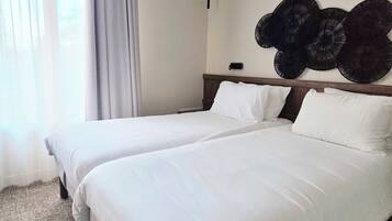 A hotel room with two beds, a large window with sheer curtains, and a wall-mounted decorative item.