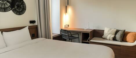 A hotel room with a large bed, a desk with a chair, and a sofa with cushions.