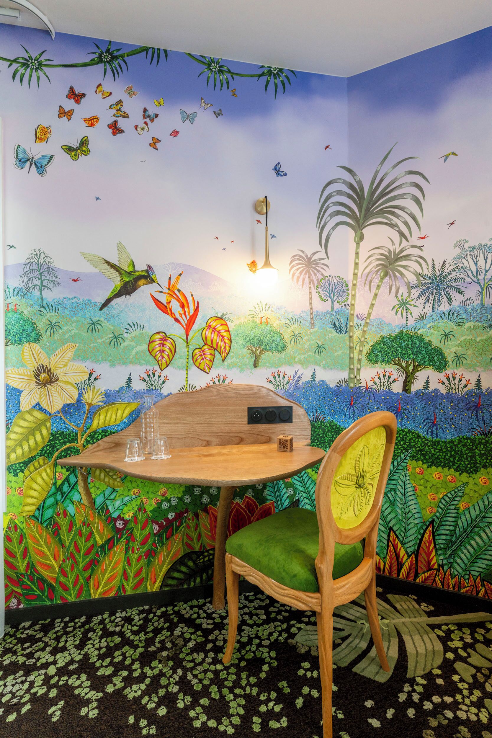 A room with a mural of a tropical landscape, a wooden table with a chair, and a small plant on the table.