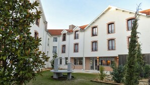 A courtyard with a stone bench, a small tree, and a building with multiple windows and a brick facade. - The Originals Boutique Hotel Rivella (Clisson)