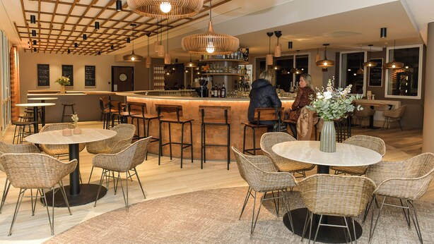 A modern bar area with wicker chairs, a central bar counter, and pendant lighting. - The Originals Boutique Hotel Rivella (Clisson)