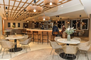 Uma área de bar moderna com cadeiras de vime, um balcão central e iluminação pendente.