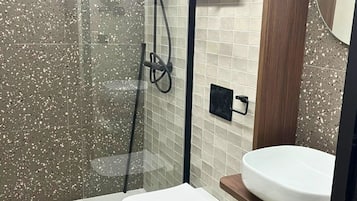 Een moderne badkamer met een douche met glazen wand, een wit toilet en een houten wastafelmeubel met een wastafel.