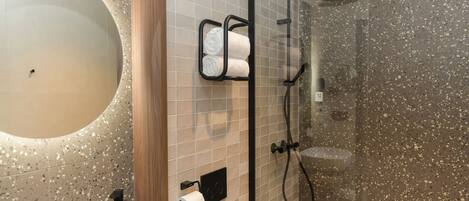 A modern bathroom with a freestanding bathtub, a glass-enclosed shower, and a toilet paper holder with towels.