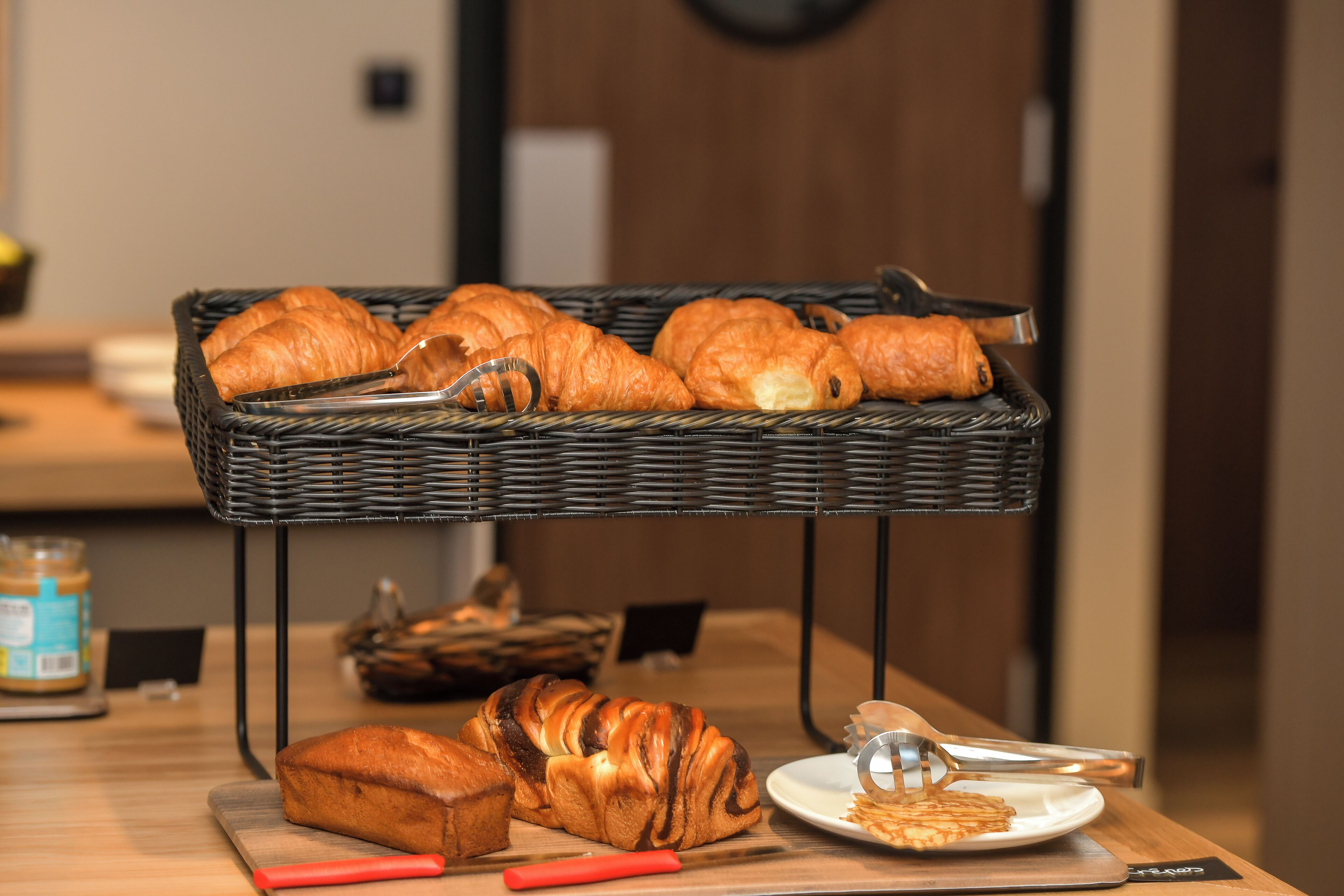 Une table en bois dressée pour le petit-déjeuner, avec des croissants, une miche de pain et une assiette sur laquelle se trouve une pâtisserie.